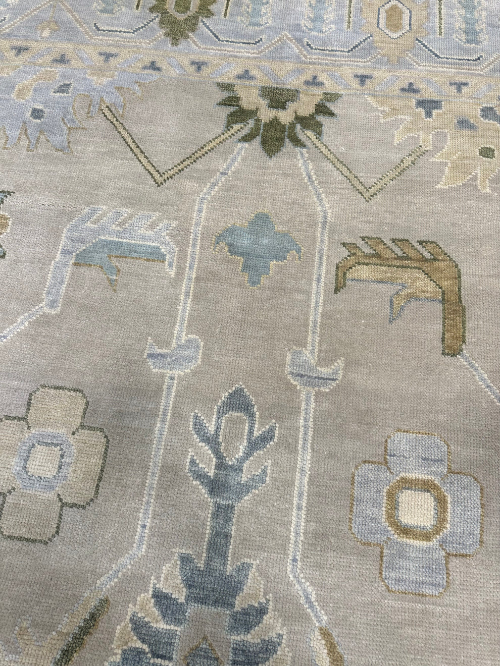 A close-up of a traditional patterned rug with a beige base and motifs in muted blue, gray, and olive green.