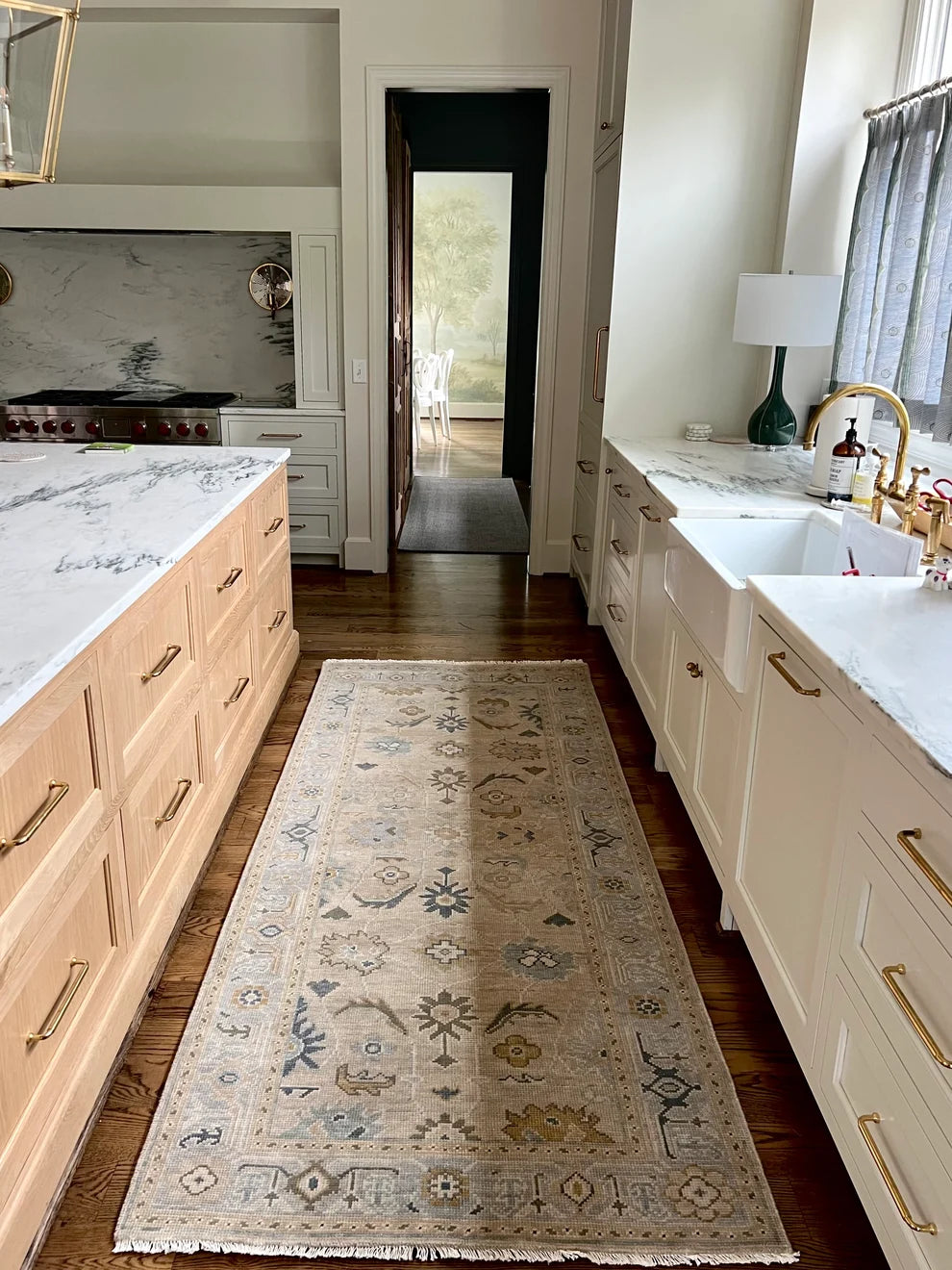 A long rectangular area rug with a distressed traditional pattern in beige, blue, and muted gold, laid out on dark wood floors in a bright kitchen.