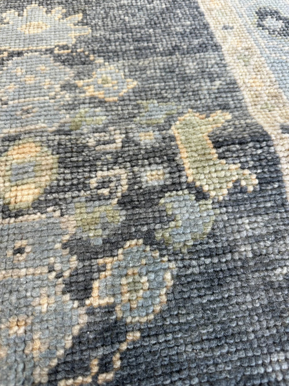 Close-up of a textured area rug with a faded traditional floral pattern in charcoal gray, slate blue, and beige.
