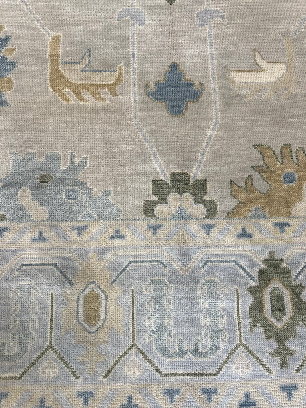 Close-up of a woven rug with a light gray-beige field and muted blue, tan, and olive geometric and animal motifs.