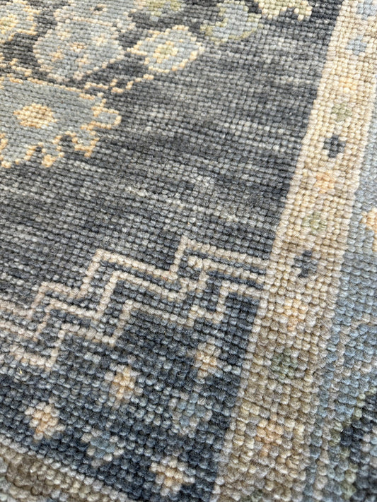 Close-up of a textured area rug with a distressed traditional pattern in slate blue, charcoal gray, and beige.