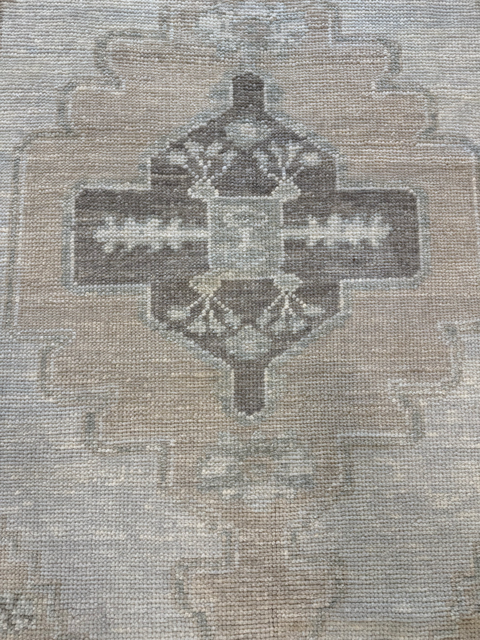 A close-up of a woven rug or textile with a muted geometric medallion pattern in taupe, beige, gray, and brown tones.