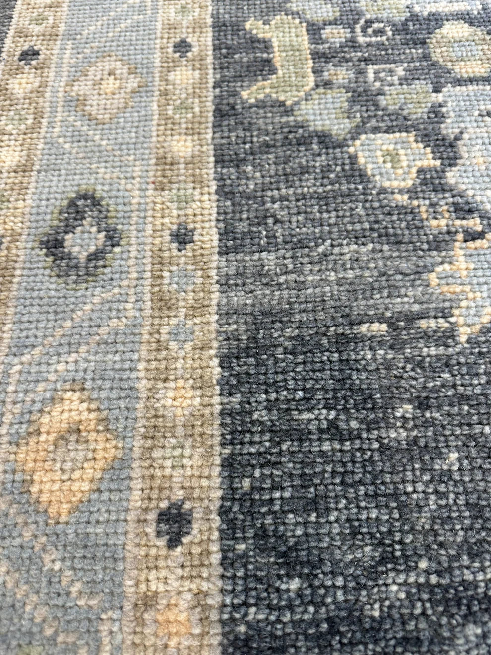 Close-up of a textured area rug showing a distressed pattern with a light blue-gray field, a beige decorative border, and a dark charcoal gray section.