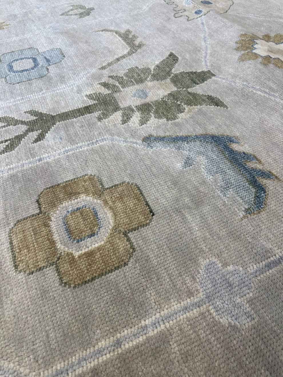 Close-up of a woven area rug with a muted floral pattern in beige, light blue, and olive green on a light gray base.
