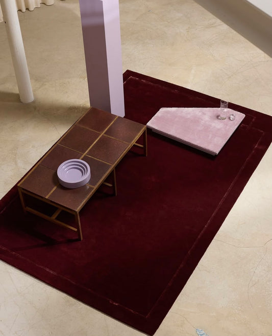 Burgundy red modern hand tufted rug with subtle tonal border styled in a contemporary living room