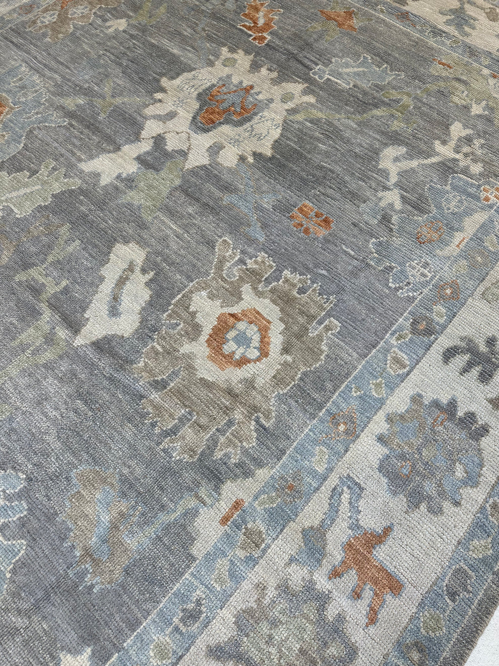 A close-up of a traditional area rug featuring a distressed floral pattern in muted shades of slate blue, beige, gray, and terracotta orange.