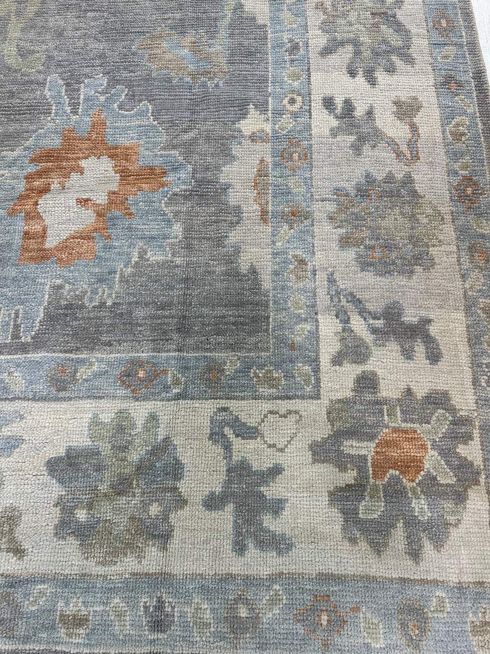 A close-up of a traditional area rug featuring a distressed blue-gray field with floral motifs in muted orange, beige, and gray.