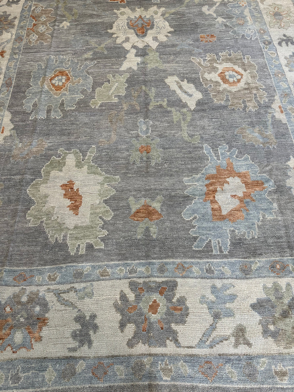 A close-up of a distressed traditional area rug featuring a muted blue-gray field with cream, light blue, sage green, and rust-orange floral motifs.